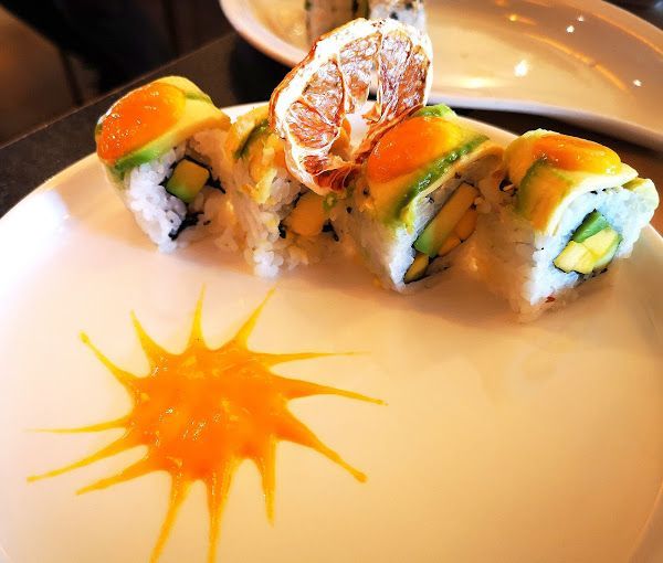 Rotolo di sushi con mango, avocado e salsa decorativa su un piatto bianco.