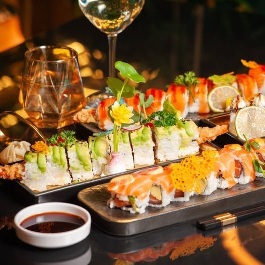 Rotoli di sushi su vassoi con una bevanda, salsa di soia e bacchette su un tavolo buio.