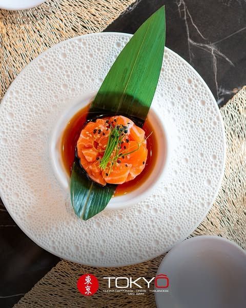 Tartare di salmone con salsa, servita su un piatto bianco con guarnizione di foglia verde.