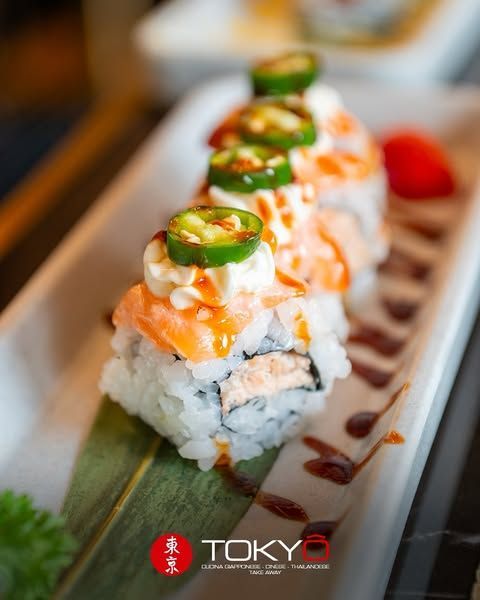 Rotolo di sushi con salmone, jalapeno e salsa, servito su un piatto bianco.