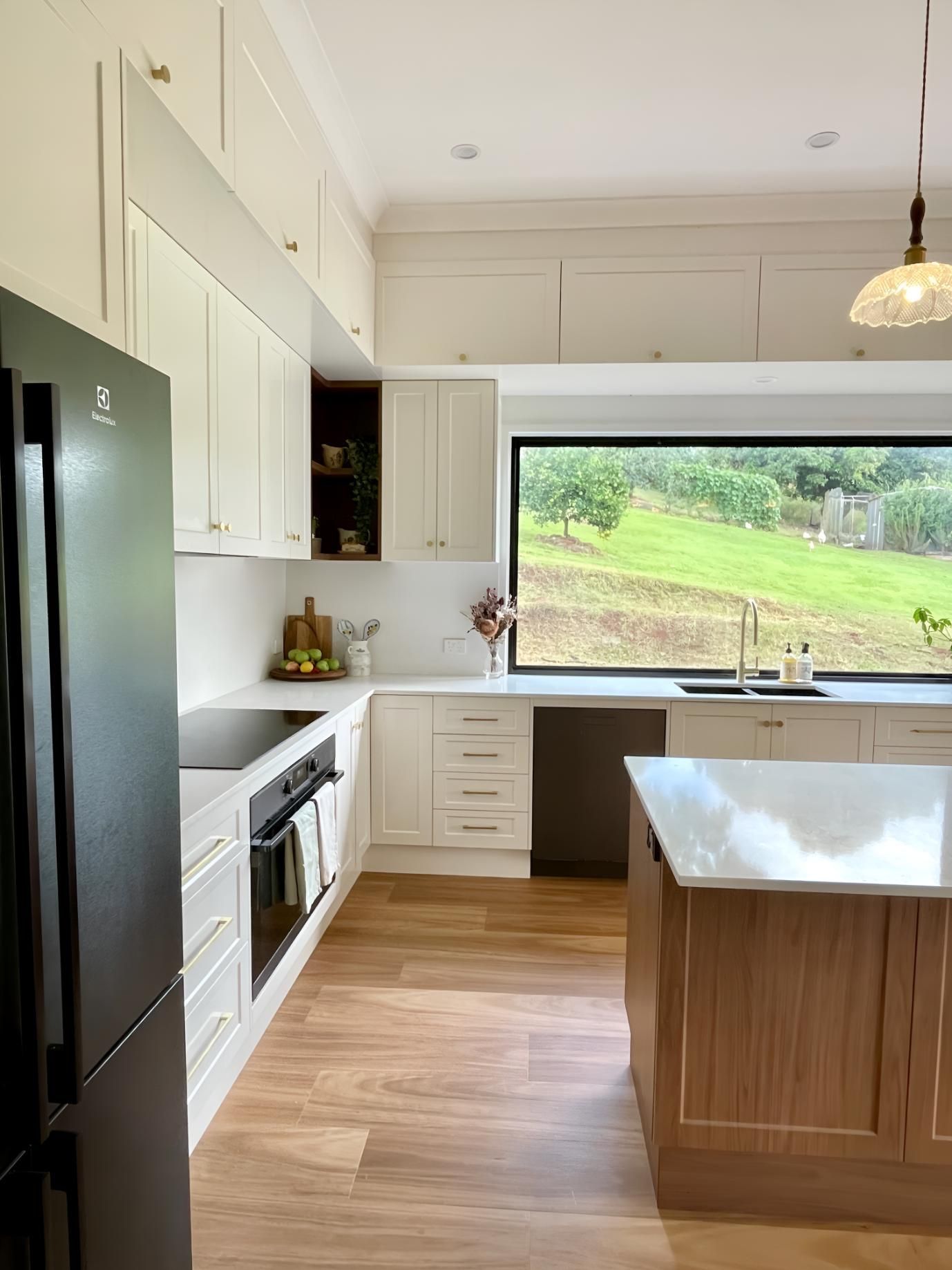 A Kitchen With White Cabinets, a Black Refrigerator and a Large Window 