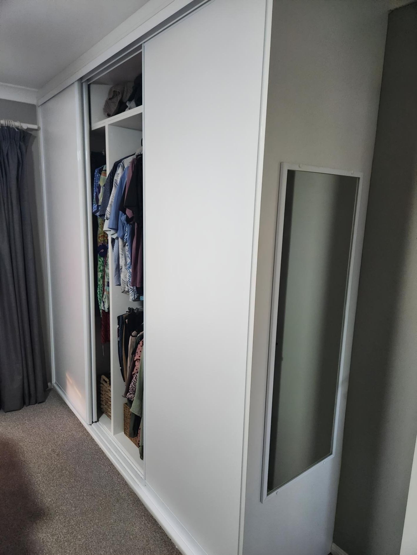 A Large White Wardrobe With Sliding Doors and a Mirror in a Bedroom — BM Cabinetry In Spring Grove, NSW