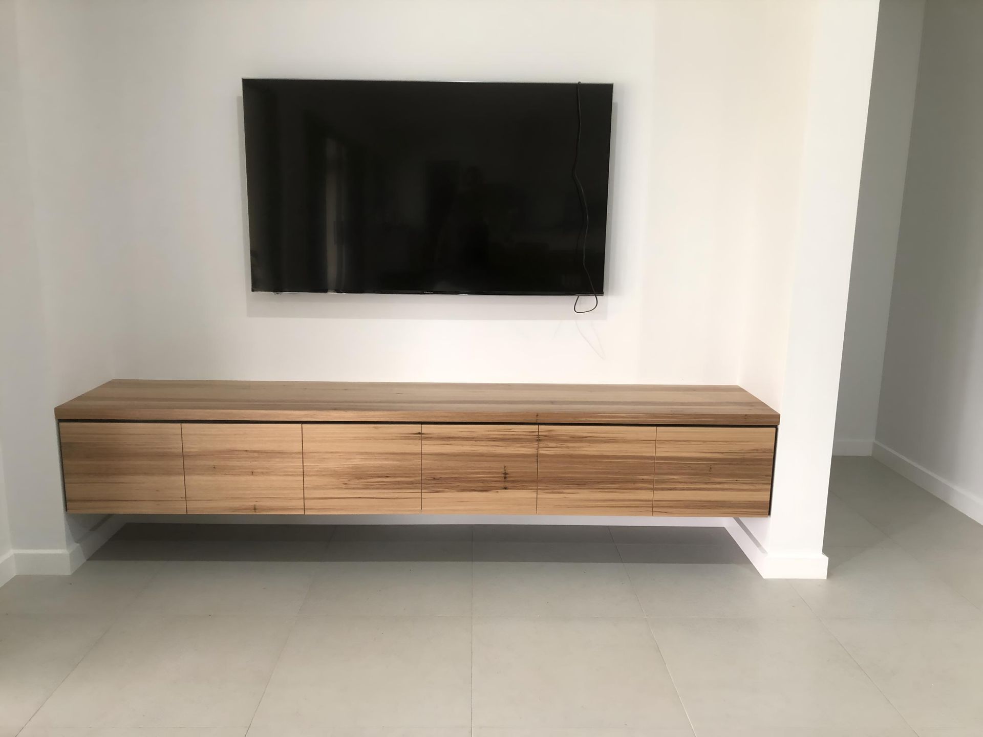 A Flat Screen Tv is Mounted to the Wall Above a Wooden Entertainment Center — BM Cabinetry In Spring Grove, NSW