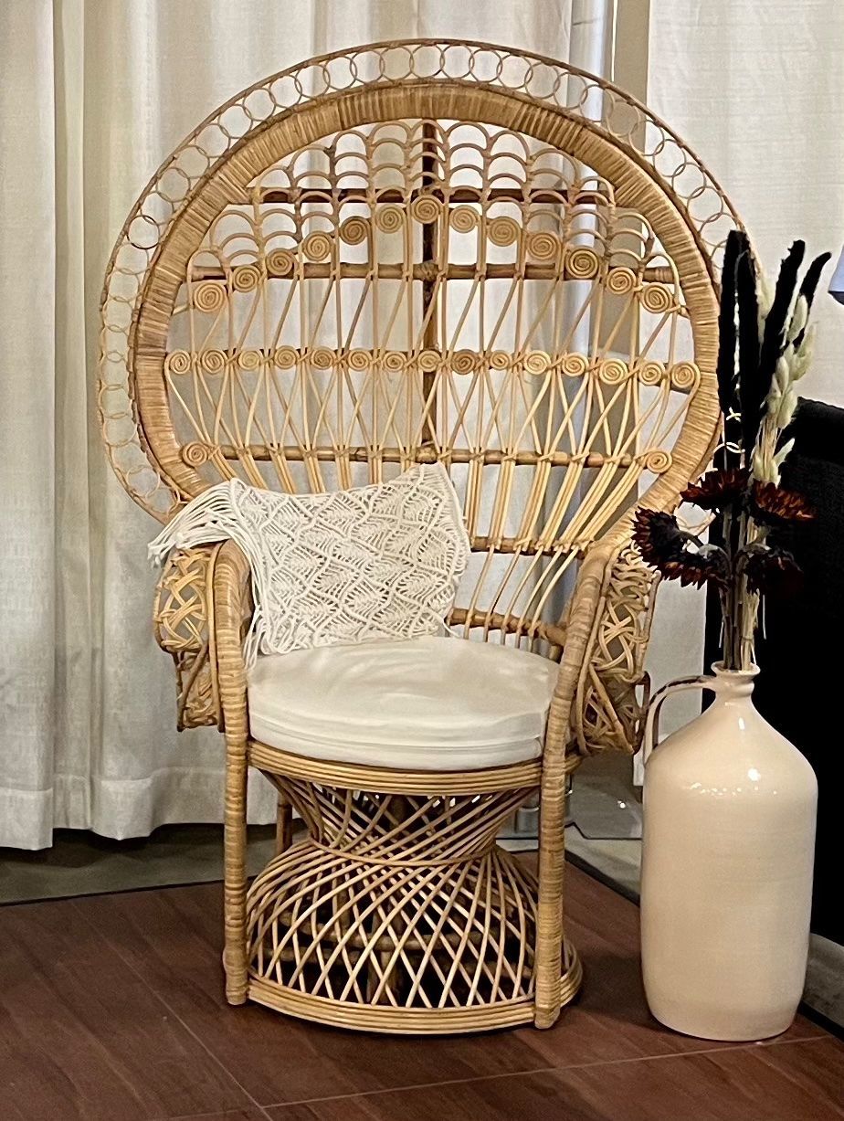 A wicker chair is sitting on a wooden floor next to a vase of flowers.