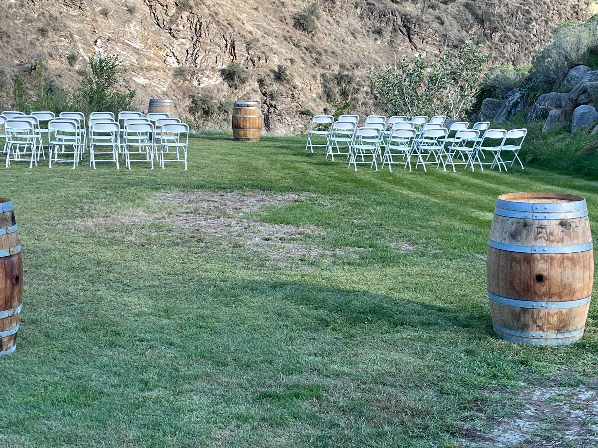 A row of chairs and wooden barrels in a grassy field.