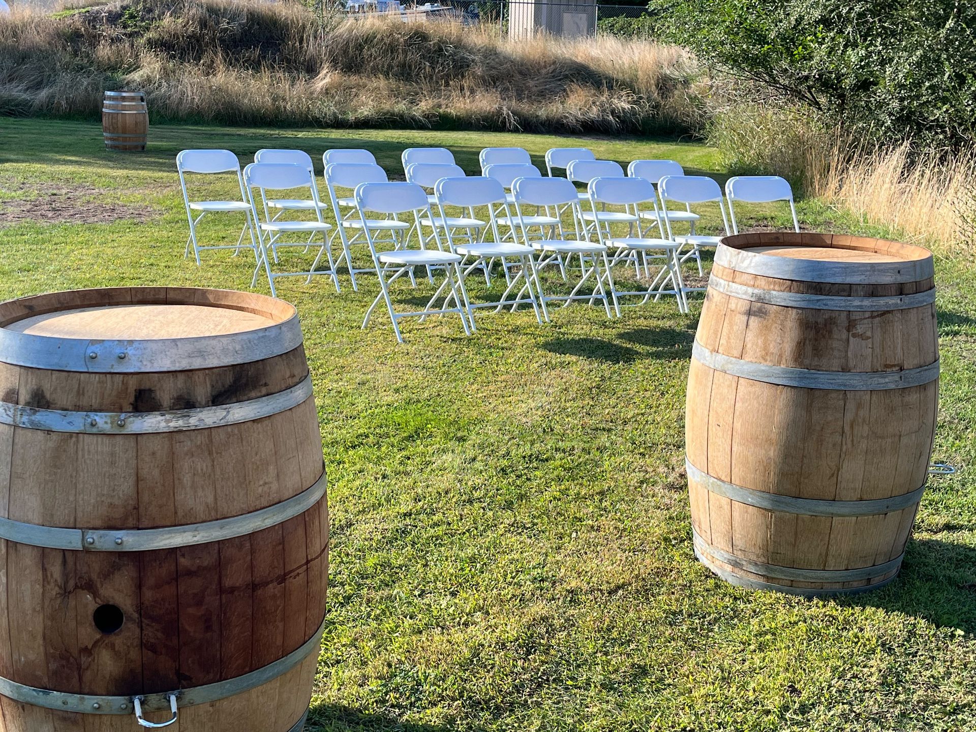 Two wooden barrels are sitting in the grass next to a row of folding chairs.
