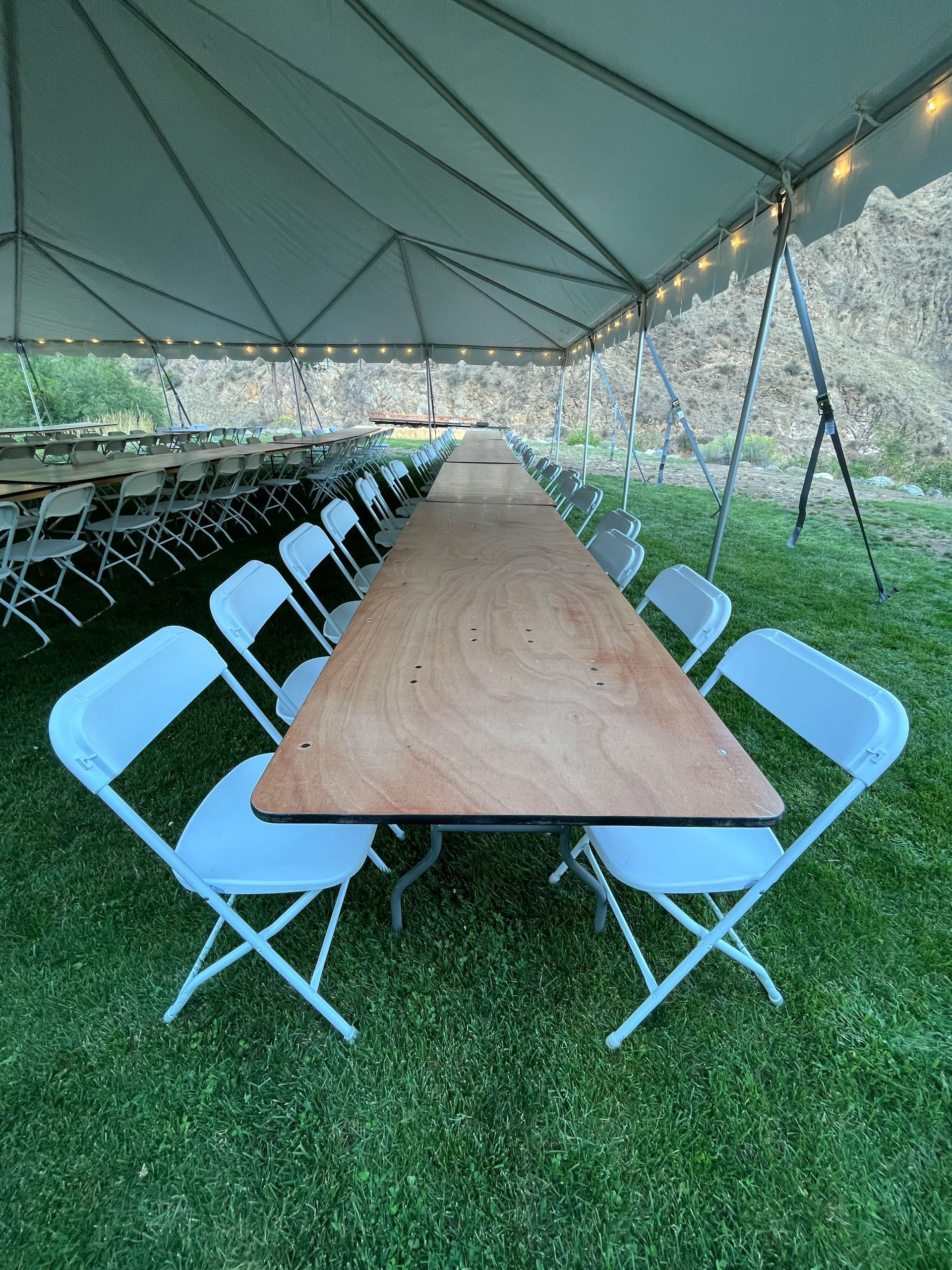 A long wooden table with white chairs under a tent.