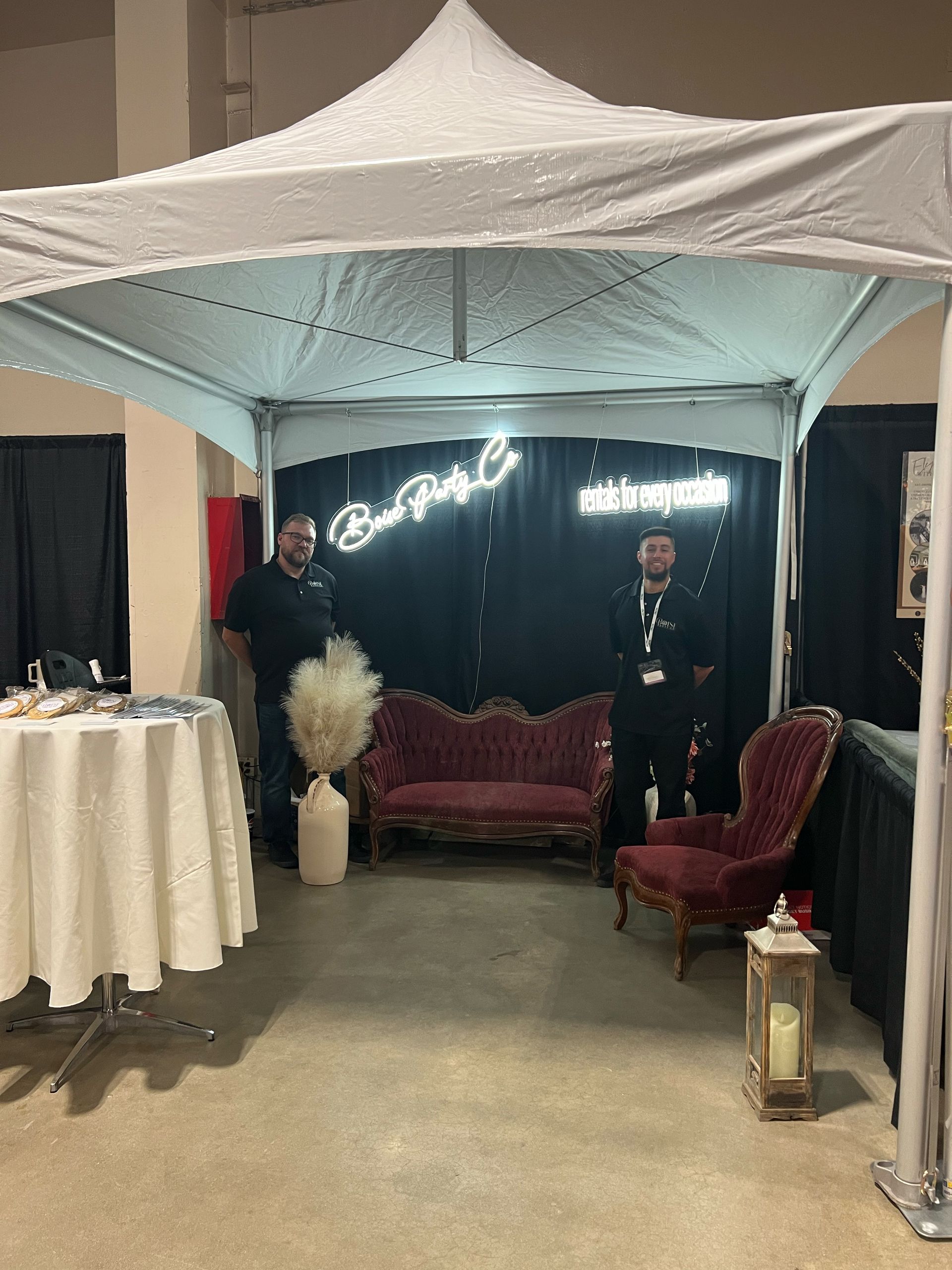 Two men are standing under a tent in a room with a couch and chairs.