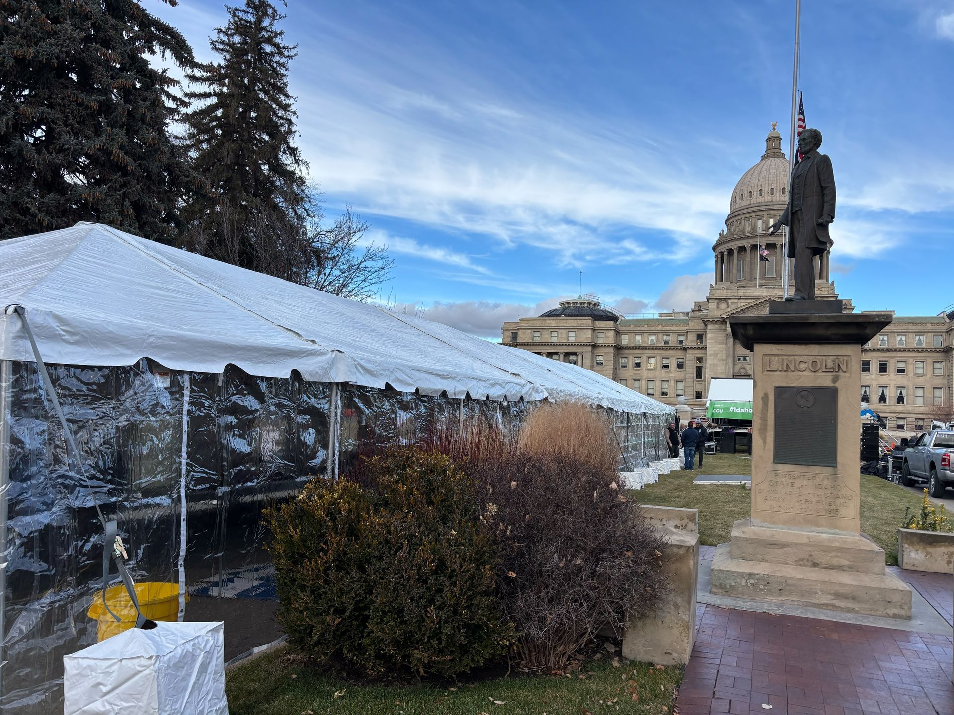 A statue of a man standing in front of a building with a tent in the foreground.