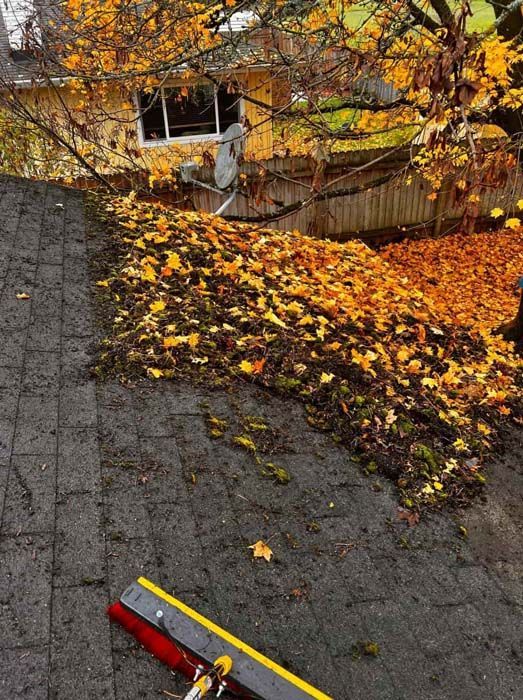 A broom is sitting on a roof next to a pile of leaves.