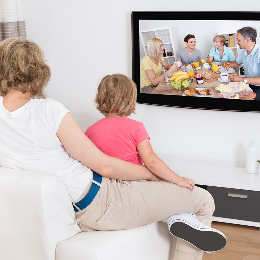 A family is sitting on a couch watching a slideshow on a television
