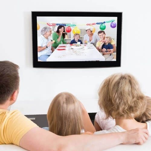 A family is watching a birthday party pictures on television