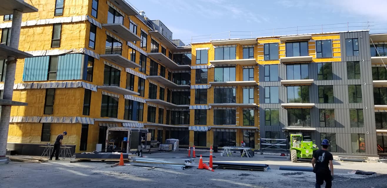 Construction d'un immeuble à plusieurs étages. L'extérieur présente une isolation jaune, des fenêtres et des ouvriers.