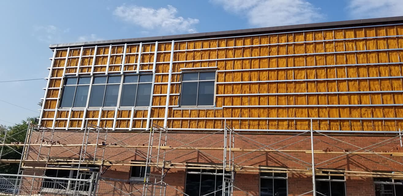 Bâtiment en construction, mur partiel recouvert d'isolant, échafaudage, fenêtres, ciel bleu.