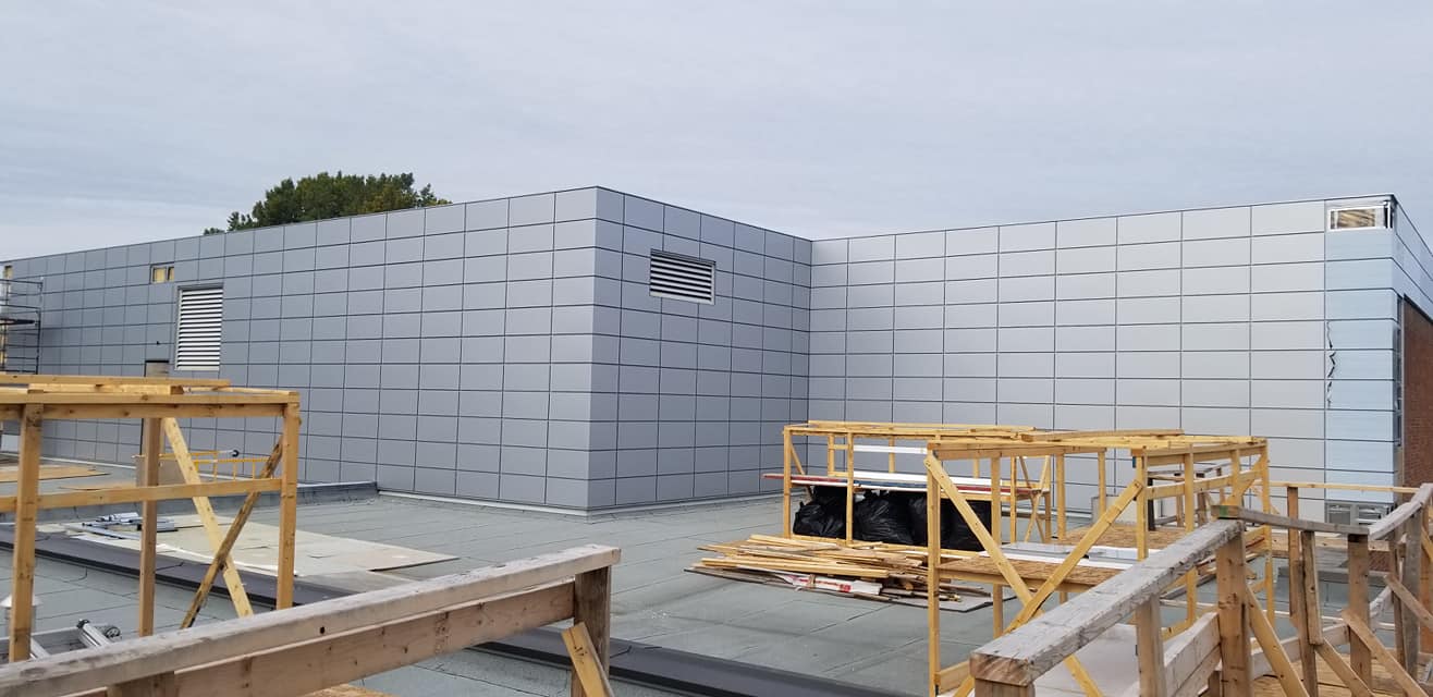 Extérieur du bâtiment en construction avec lambris argentés et échafaudages en bois. Ciel couvert.
