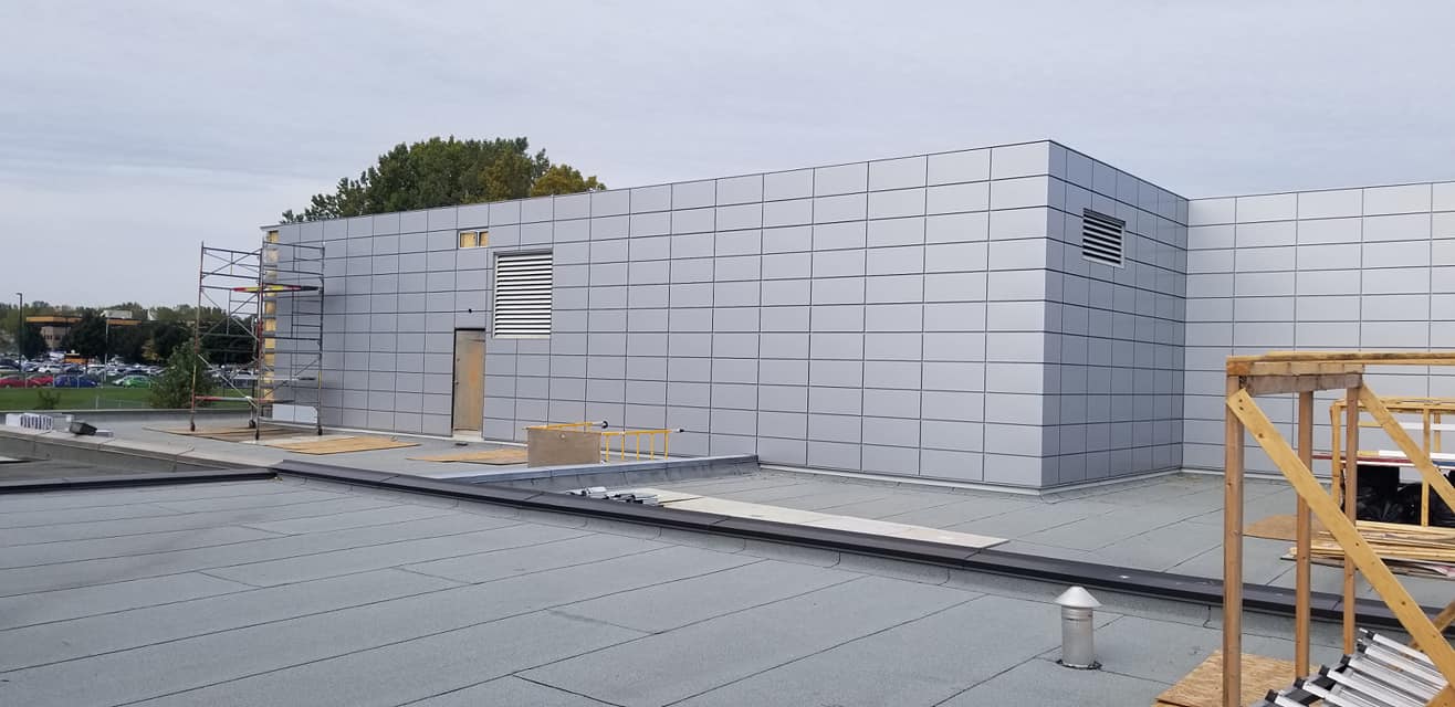 Extérieur du bâtiment en construction avec revêtement en panneaux métalliques.