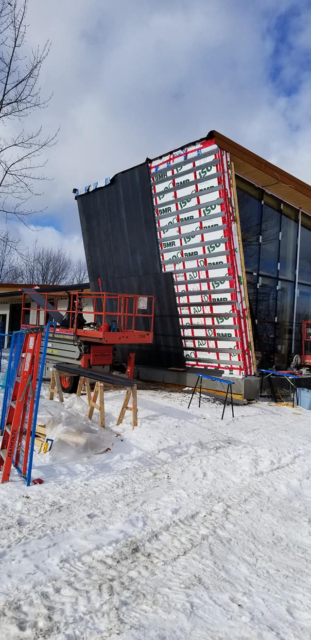 Chantier avec un bâtiment partiellement construit, un sol enneigé et un ascenseur.