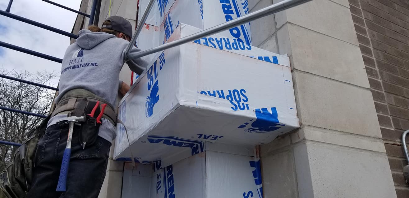 Un ouvrier du bâtiment installe une isolation en mousse sur la façade d'un bâtiment.