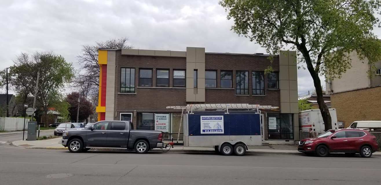 Un bâtiment en briques de deux étages avec un camion et une remorque garés devant par une journée nuageuse.