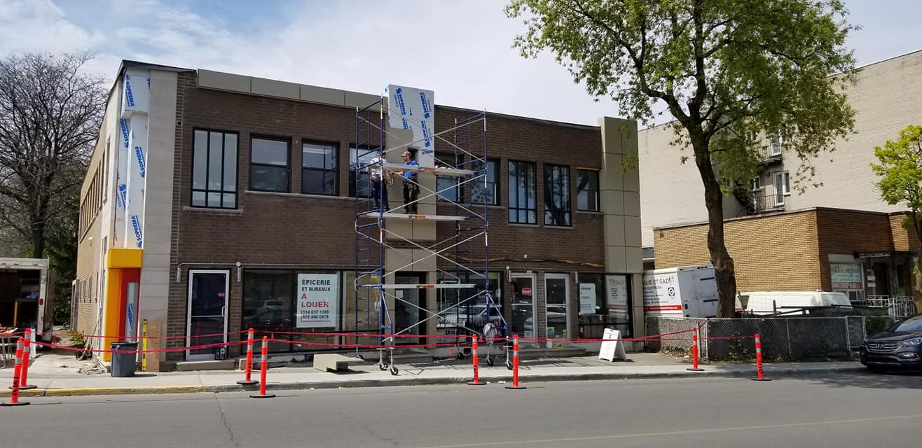 Bâtiment en construction dans une rue, avec échafaudages et cônes de sécurité.