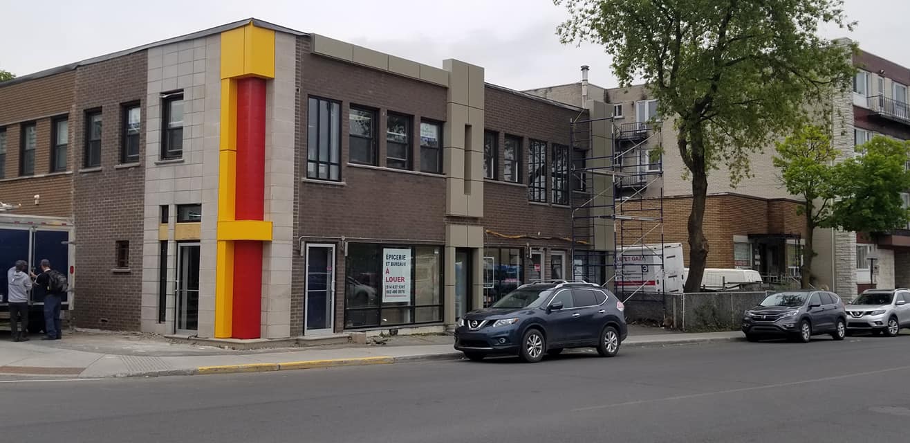 Un bâtiment en briques de deux étages au coin d'une rue avec une façade colorée et des voitures garées.