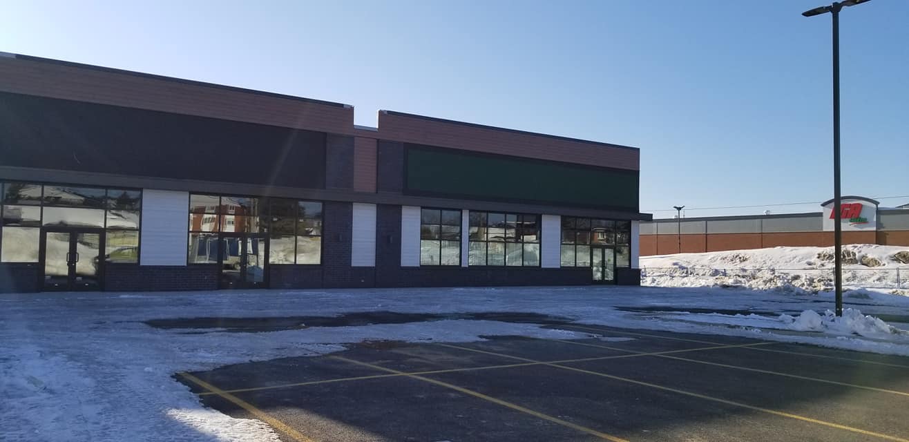 Extérieur d'un magasin par une journée d'hiver ensoleillée, avec un parking enneigé.