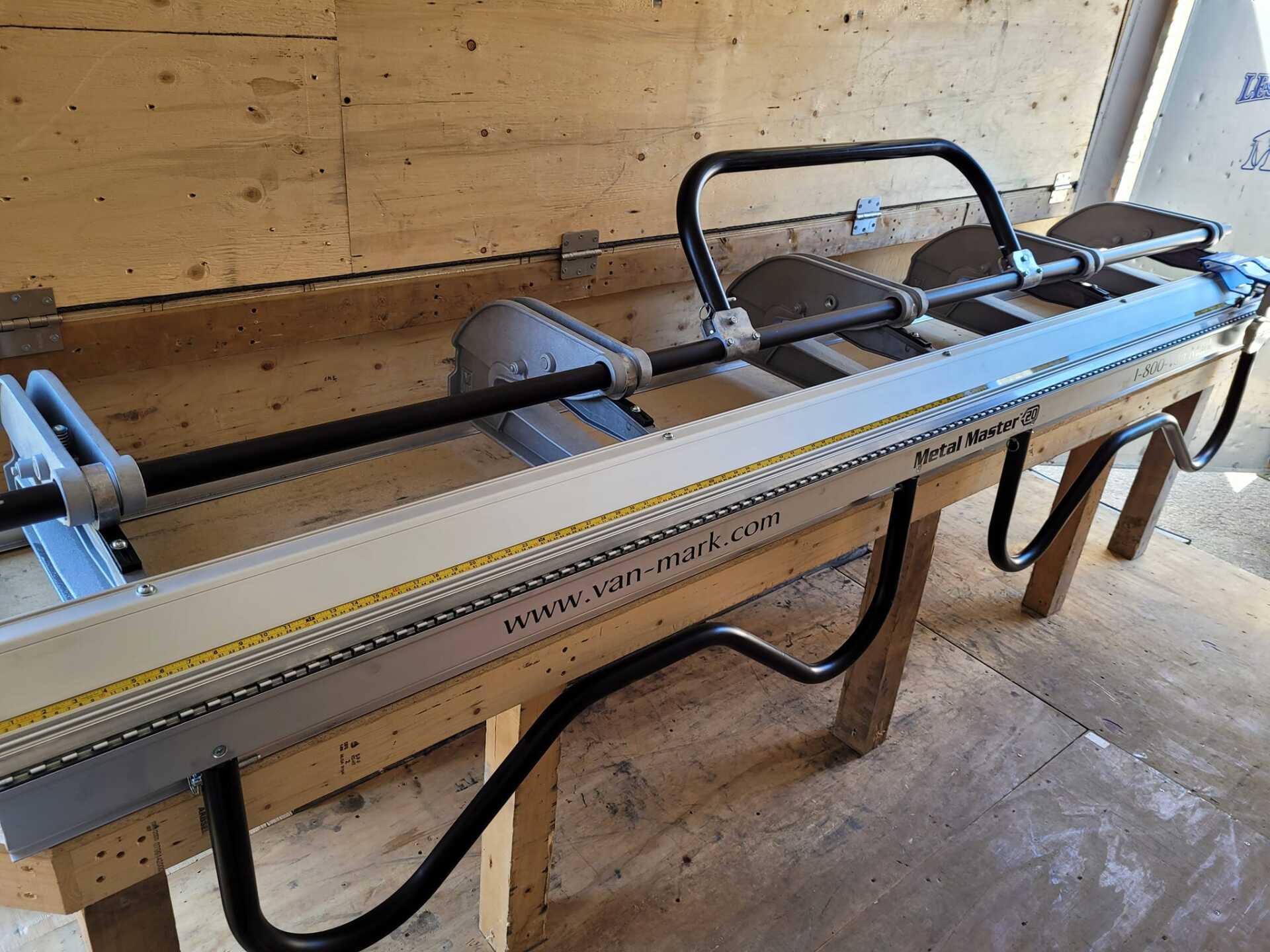 Machine à cintrer le métal sur une table en bois, dotée de leviers, de poignées et d'une longue lame.