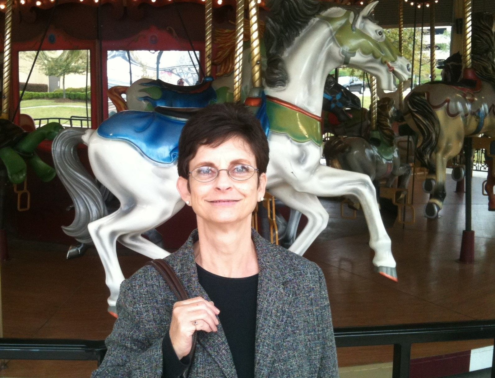 A woman stands in front of a merry go round with horses