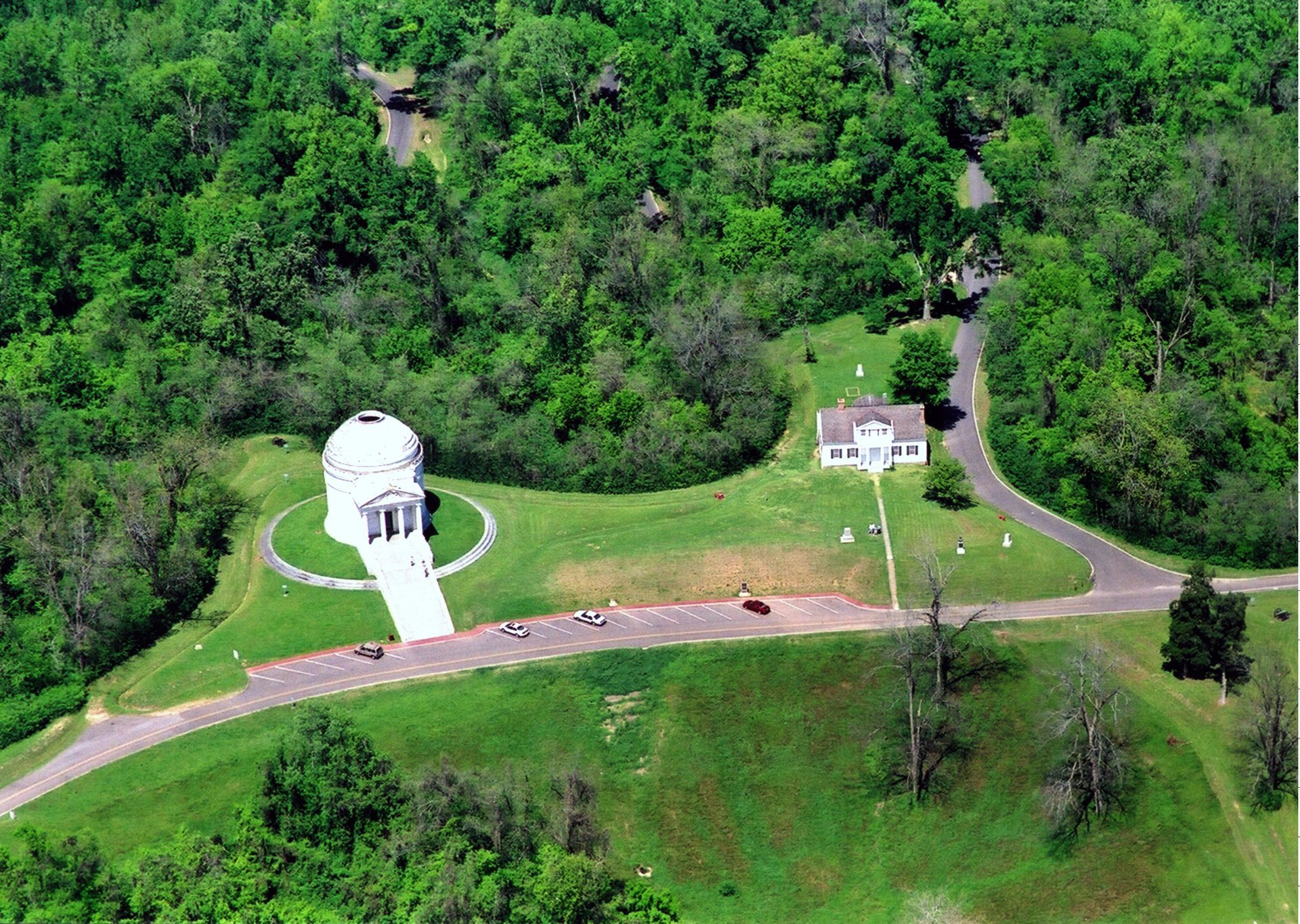 An aerial view of a house in the middle of a lush green forest