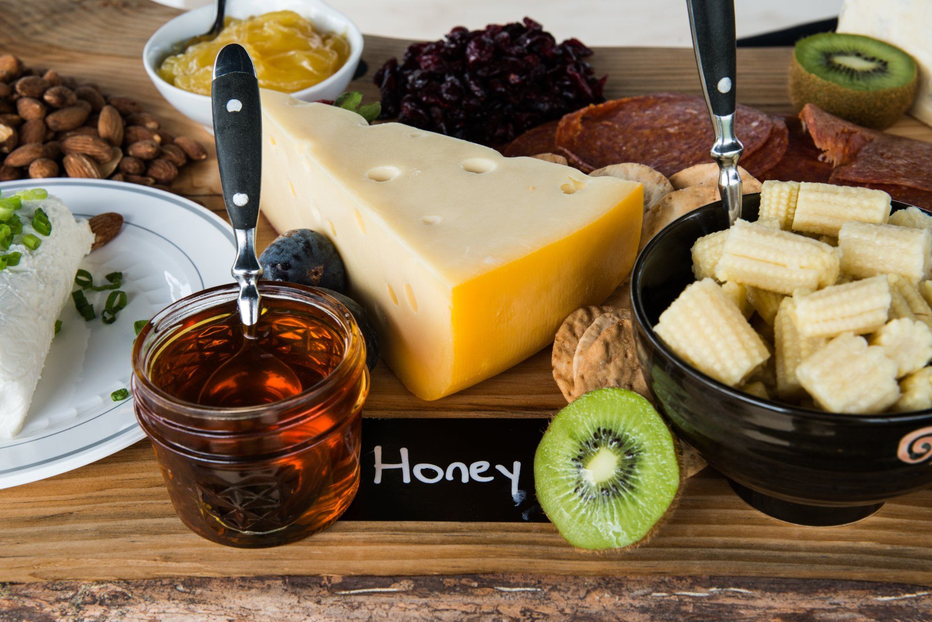 Luncheon cheeseboard with swiss, local honey, kiwis, fresh fruit preserves, aged meats, and almonds.