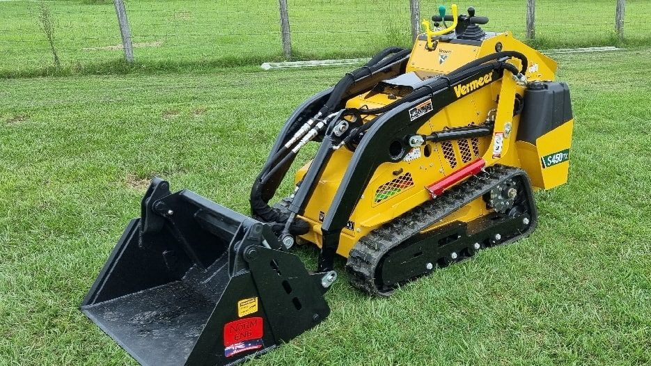 A small yellow tractor with a black bucket is sitting on top of a lush green field. — Beaudesert Equipment Hire Services in Beaudesert, QLD