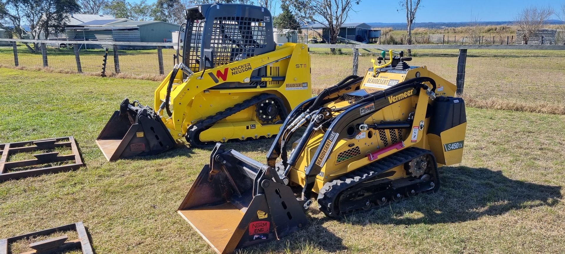 Two yellow tractors are parked in a grassy field. — Beaudesert Equipment Hire Services in Beaudesert, QLD
