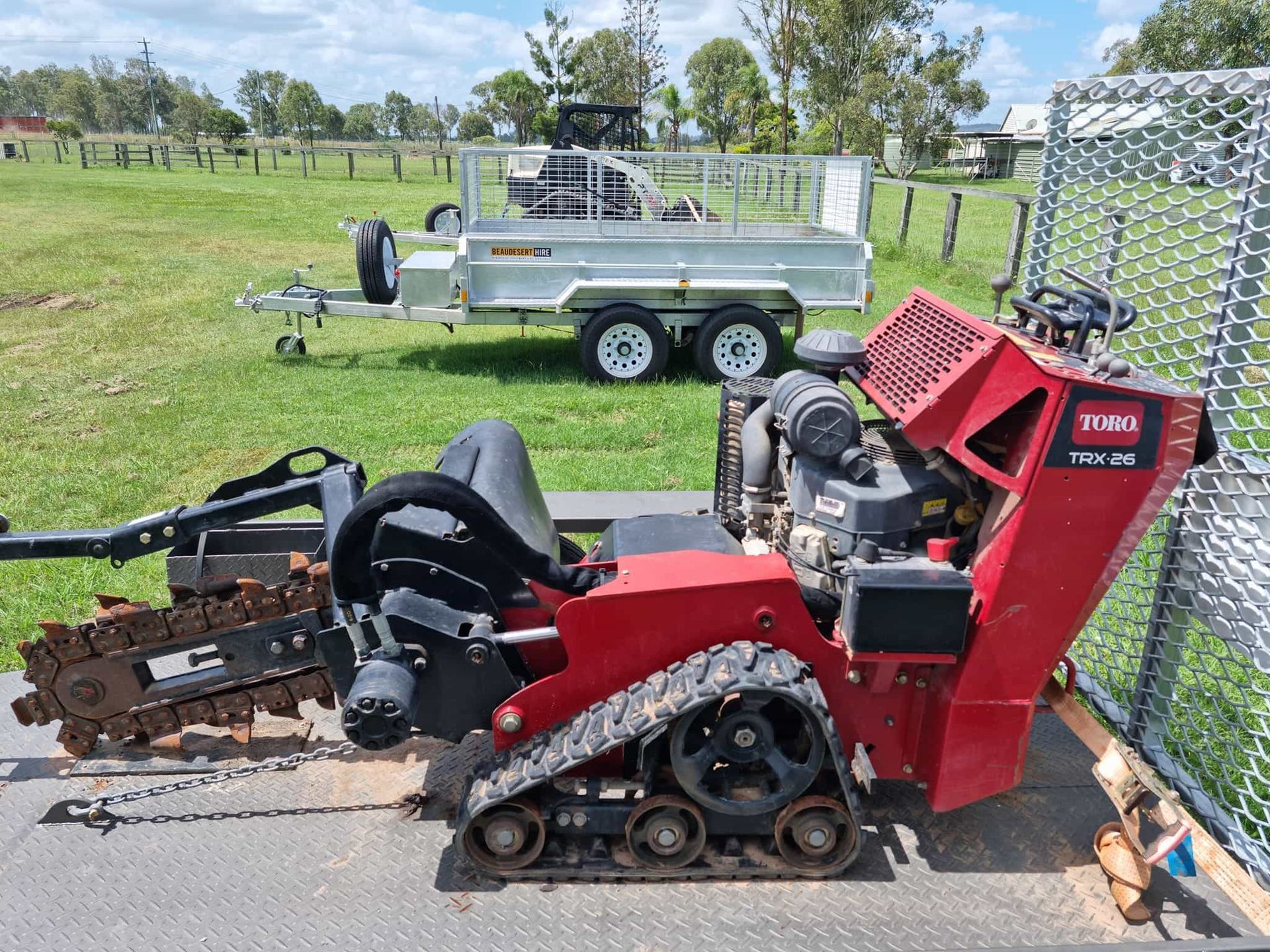 A red tractor is parked on the side of the road next to a trailer. — Beaudesert Equipment Hire Services in Beaudesert, QLD