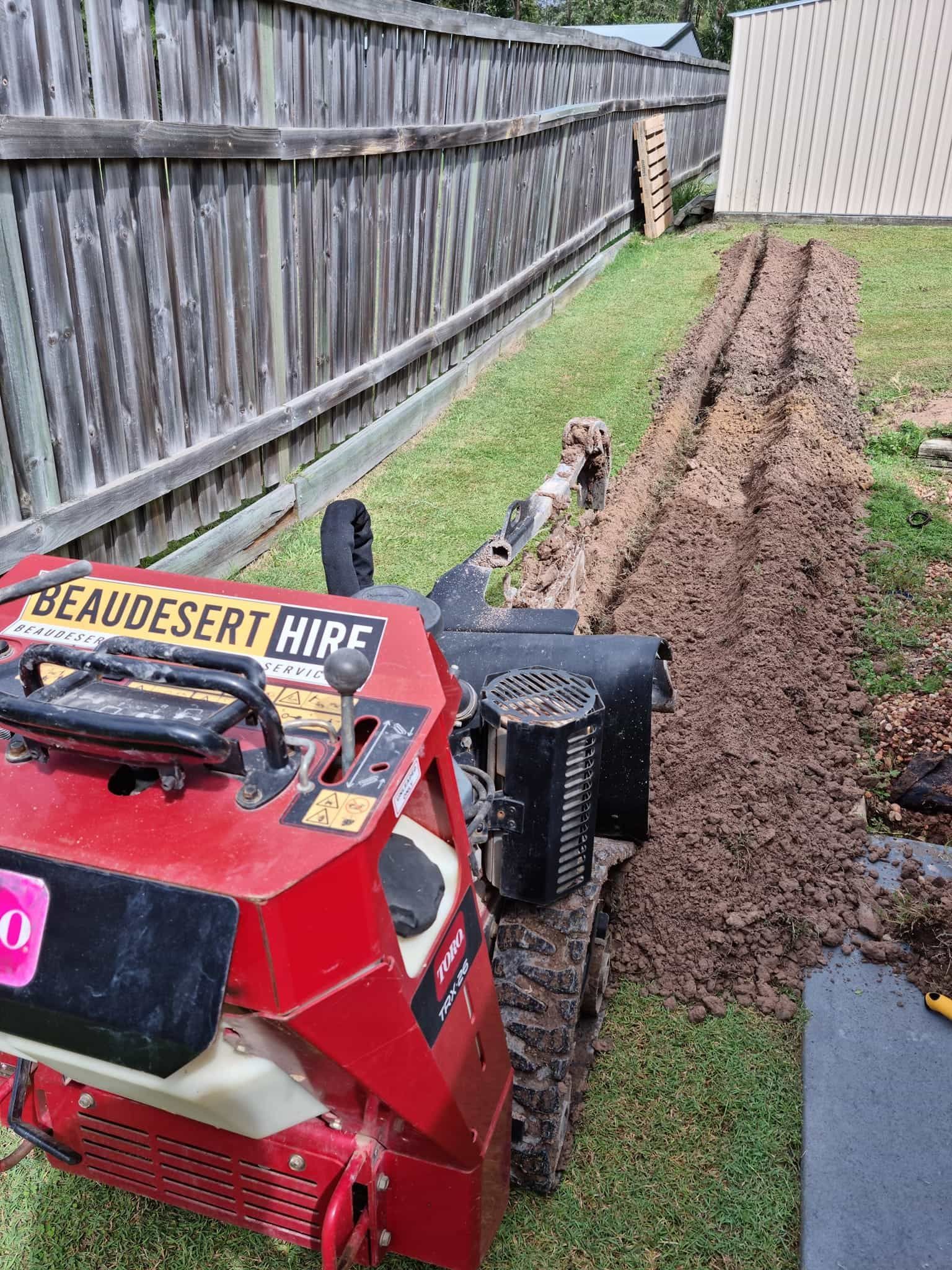 A red tractor is sitting on top of a lush green field next to a wooden fence. — Beaudesert Equipment Hire Services in Beaudesert, QLD