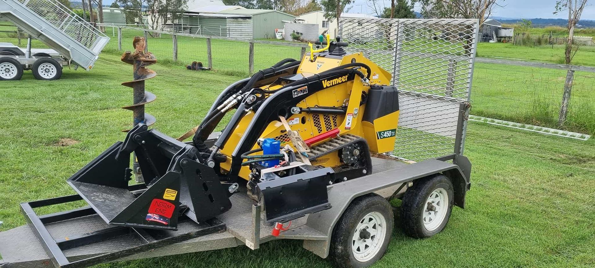 A yellow tractor is parked on a trailer in a grassy field. — Beaudesert Equipment Hire Services in Beaudesert, QLD