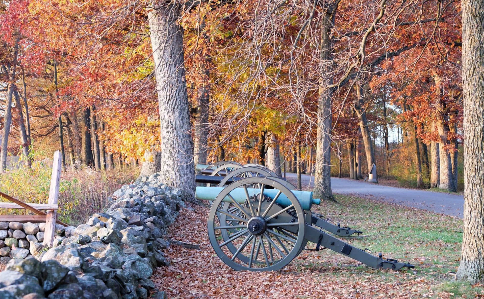 A cannon is sitting on the side of a road next to a stone wall.