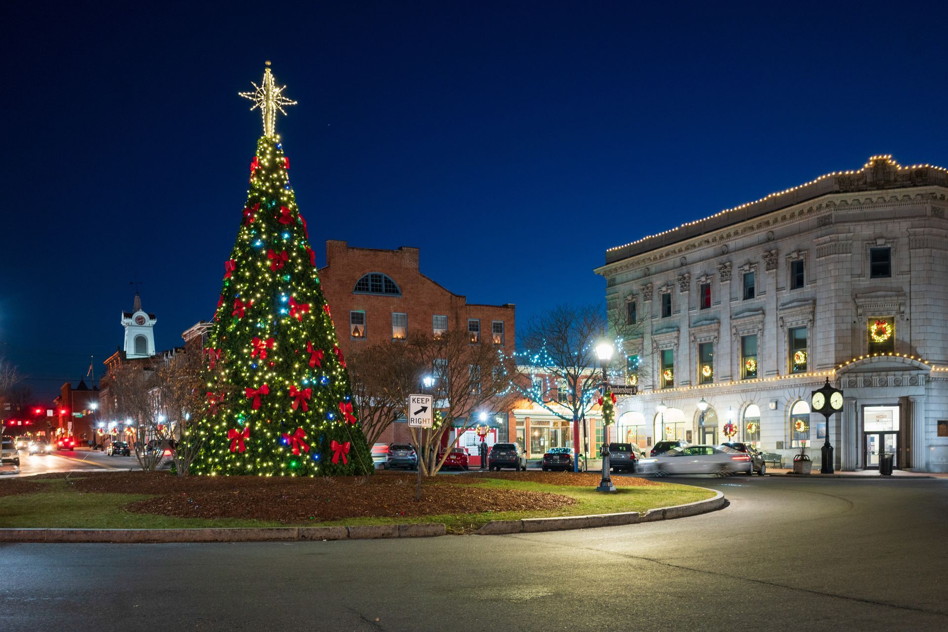 A large christmas tree is in the middle of a city at night.