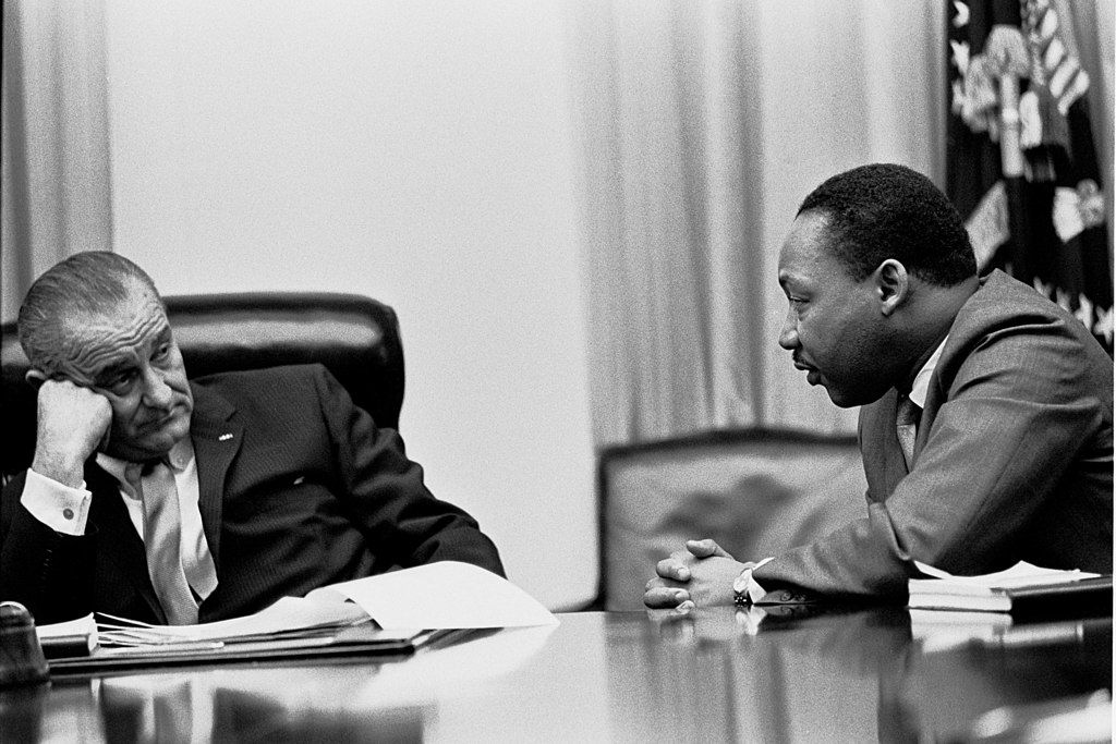 Two men are sitting at a table talking to each other