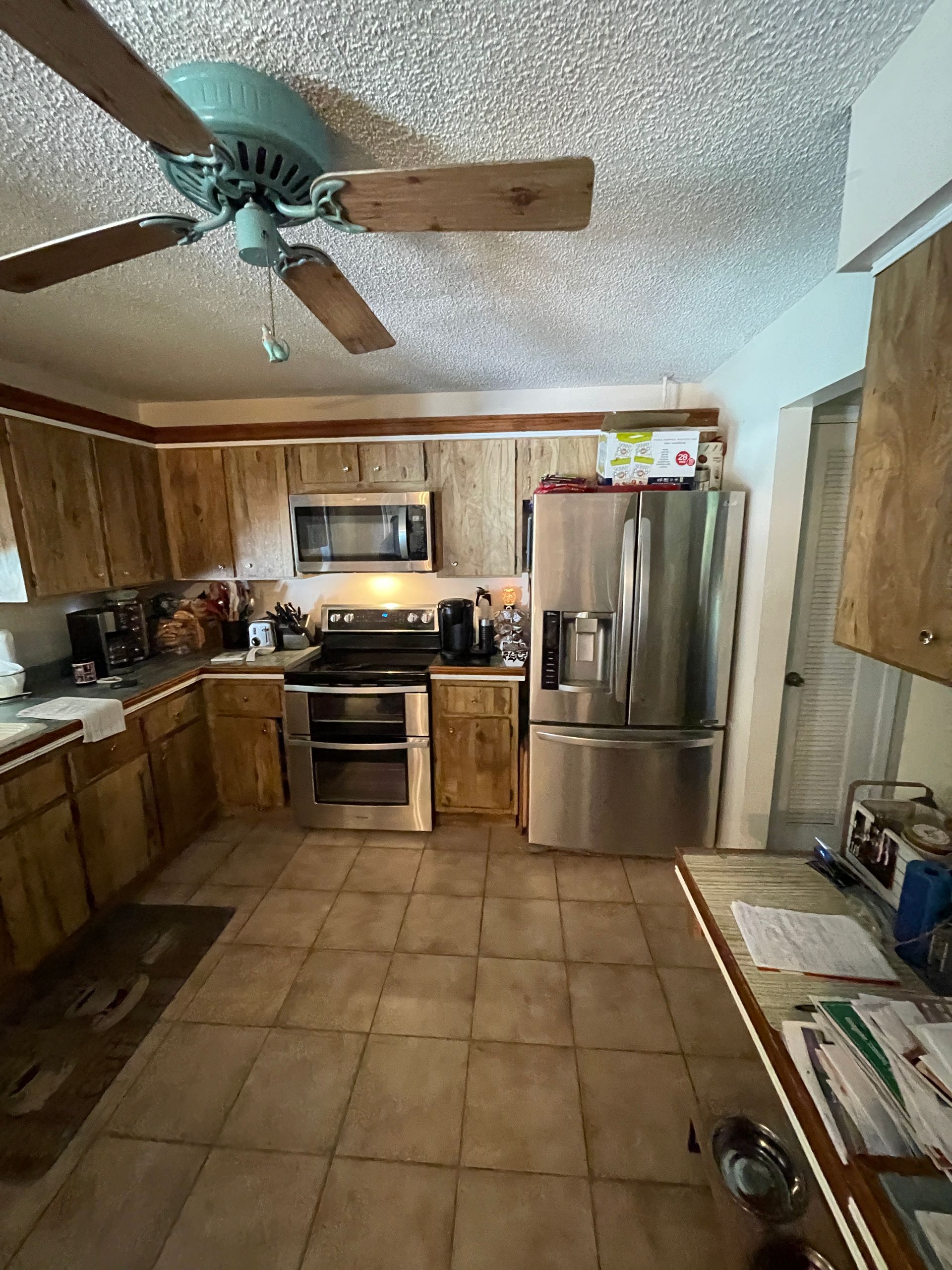 A kitchen with stainless steel appliances , wooden cabinets and a ceiling fan.