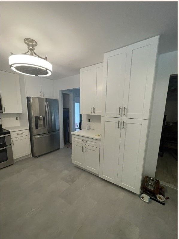 A kitchen with white cabinets , stainless steel appliances , a refrigerator and a sink.