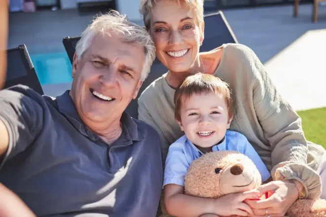 An elderly couple and a young boy are taking a selfie with a teddy bear.