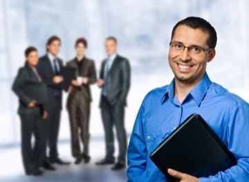 A man in a blue shirt is holding a laptop in front of a group of business people