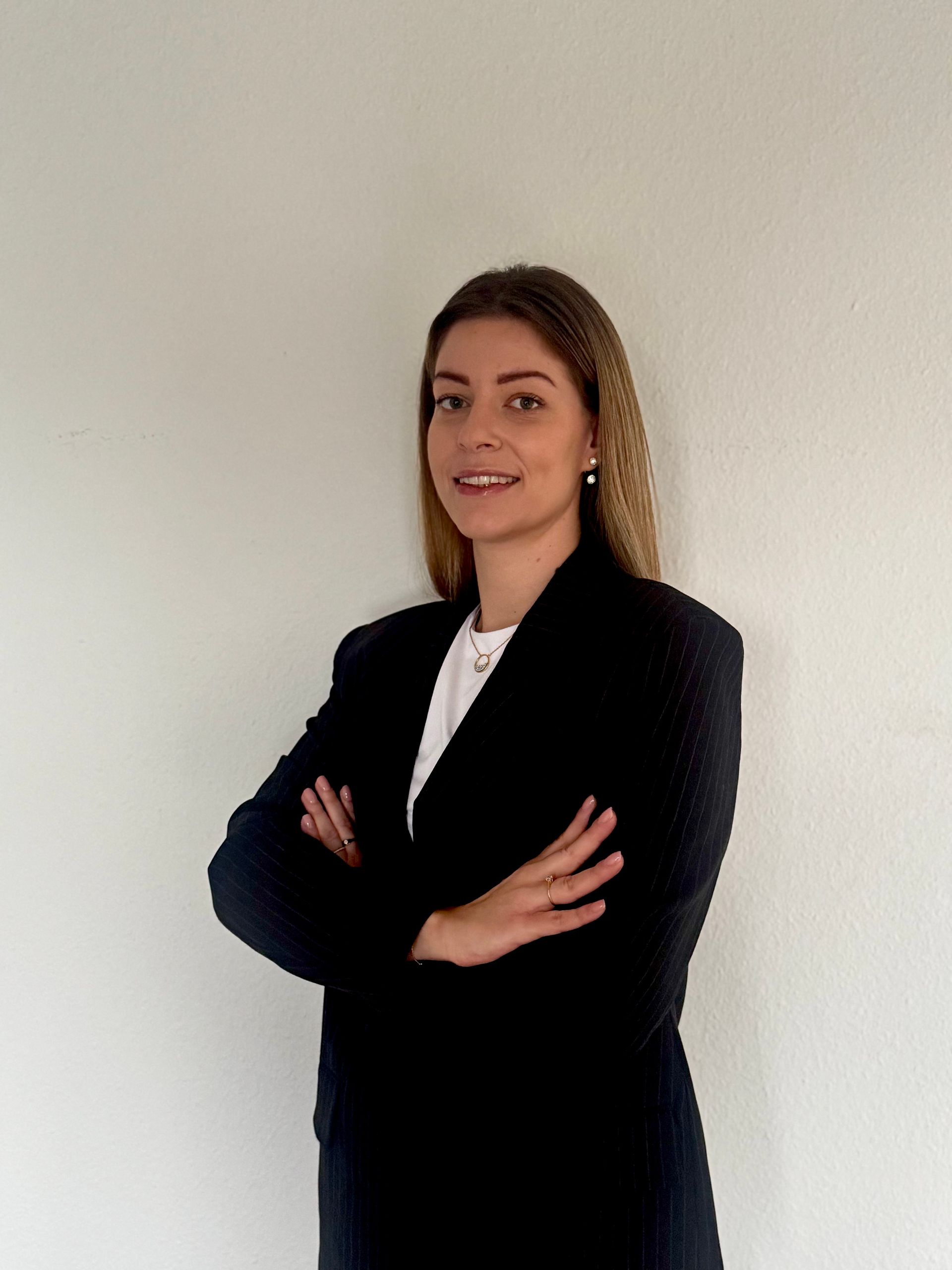 Femme en veste crème souriante, cheveux bruns, devant un mur blanc.