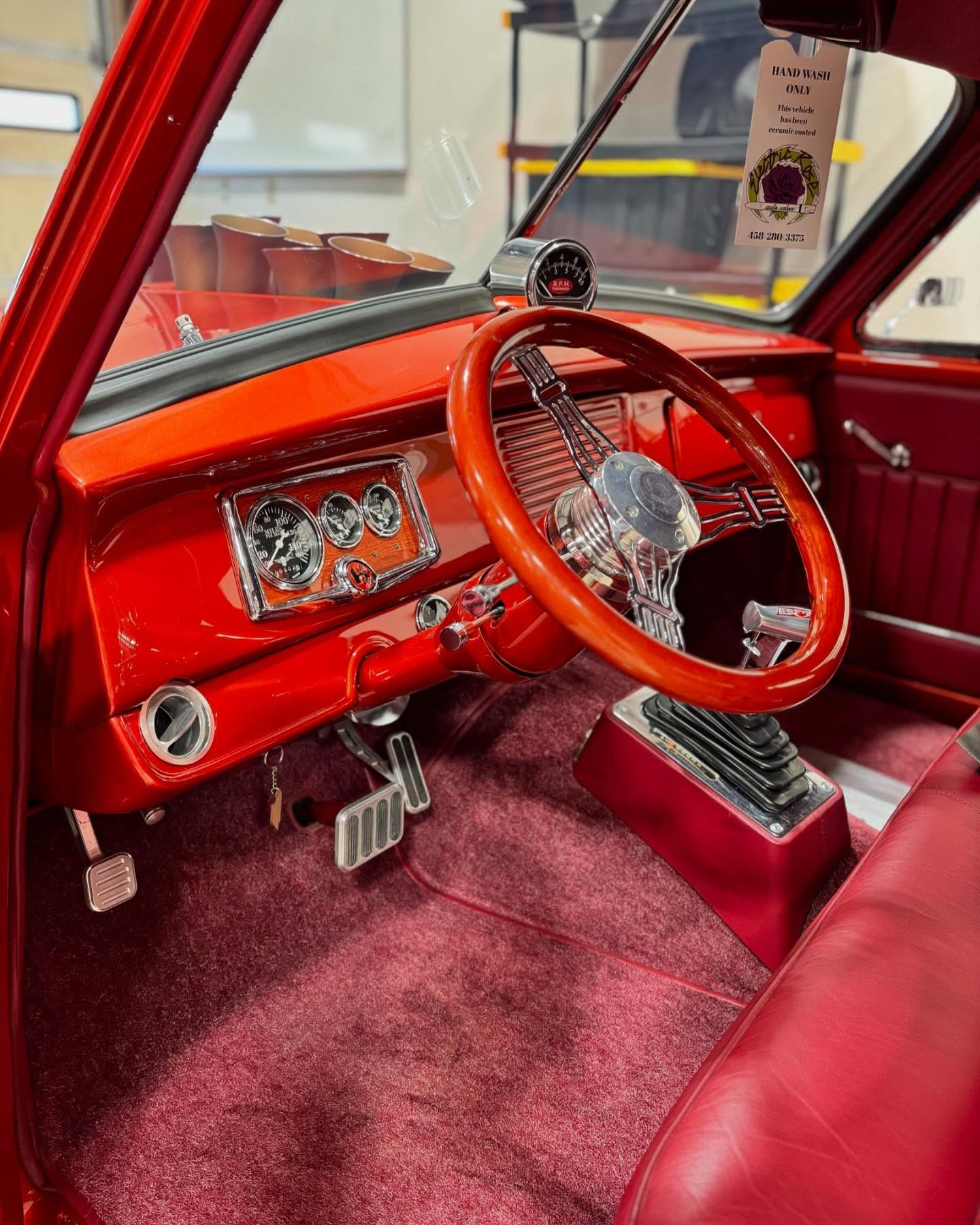 Red custom car interior with a wooden steering wheel, chrome accents, and red carpet.