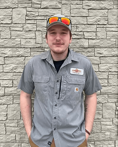 A man wearing a hat and sunglasses is standing in front of a brick wall.