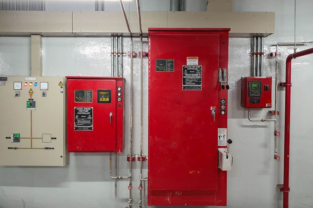 Electrical control panel equipment on a wall, including red boxes and beige panel with conduits and pipes.