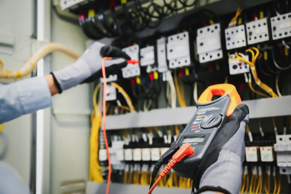 Electrician testing wires in an electrical panel with a multimeter, wearing gloves.