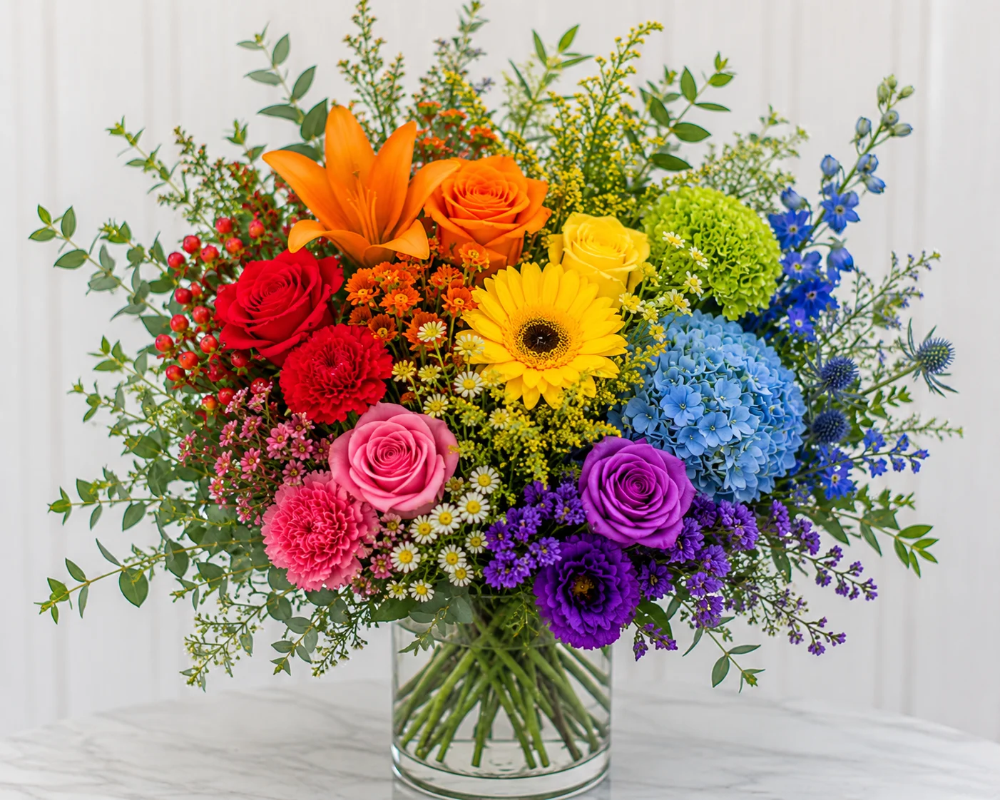 Colorful mixed flower bouquet in a glass vase with orange lilies, roses, sunflowers, and blue hydrangeas