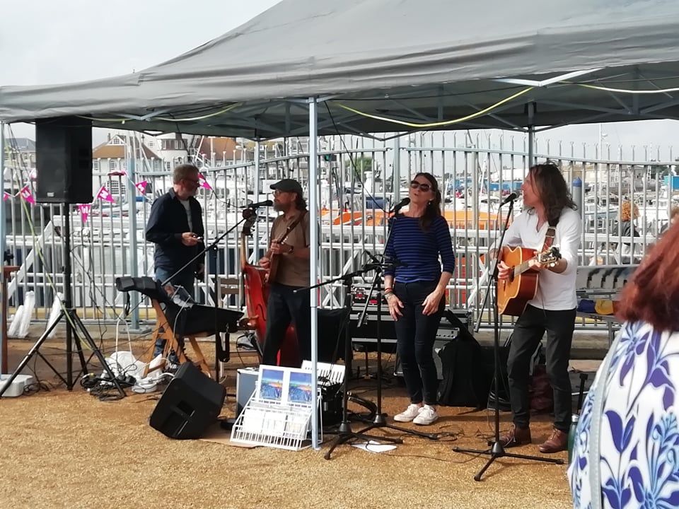 A band playing music at the fair. A lady in the middle and two guitarists playing either side of her all singing together