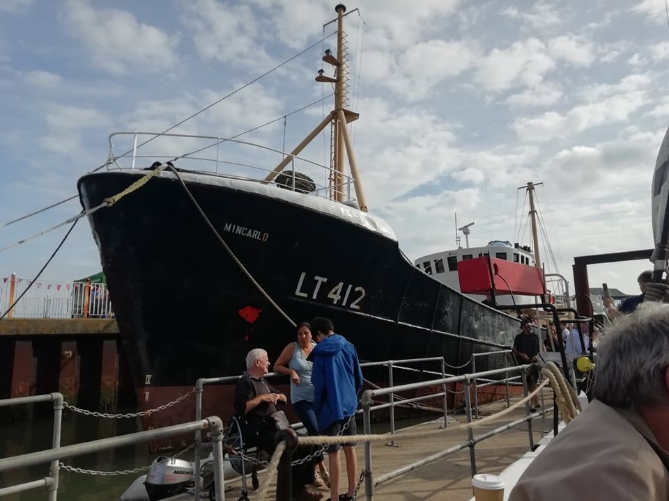 A big boat called the Mincarlo towering over a group of people relaxing